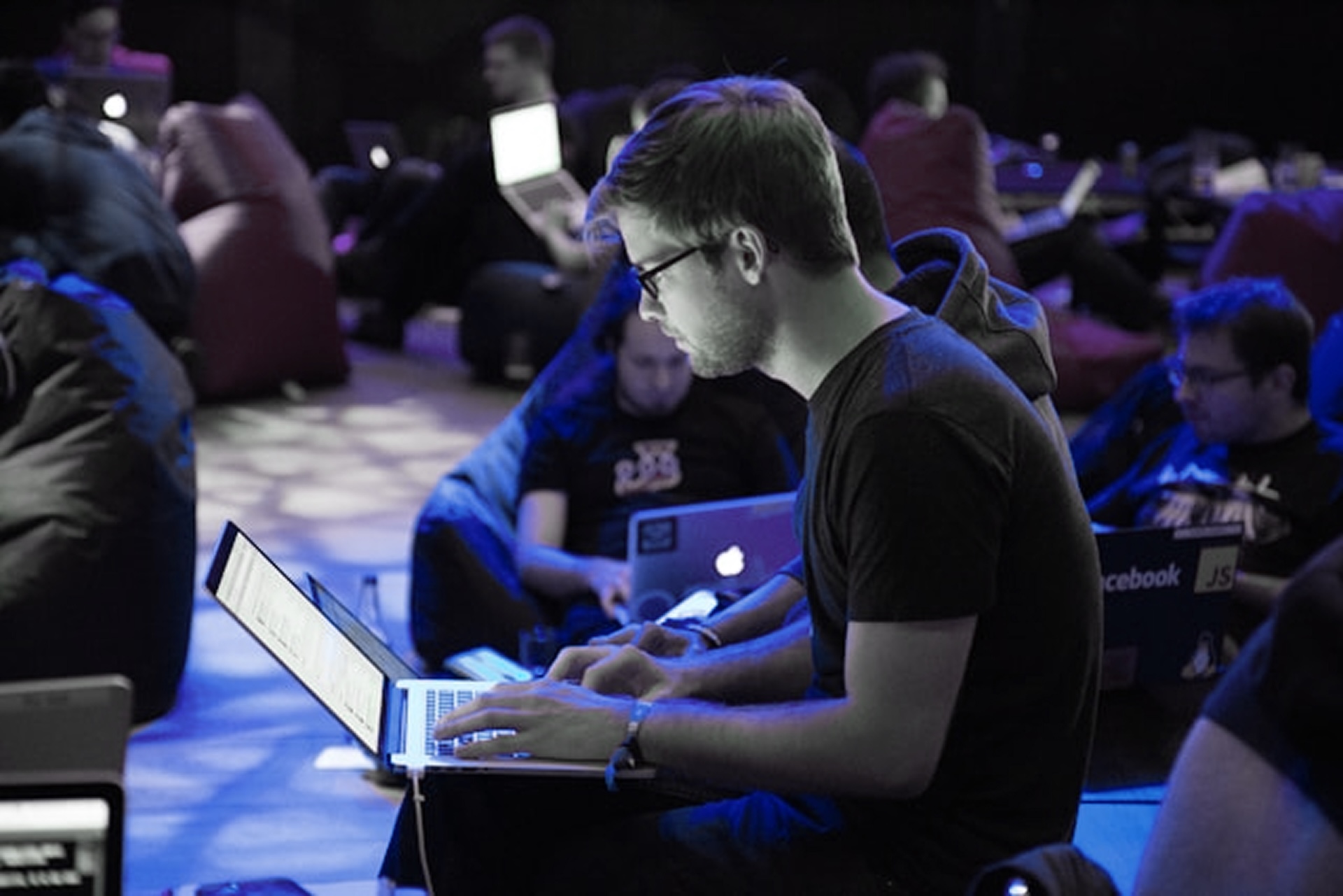 A man sitting on the ground working on a laptop with others around him doing the same.